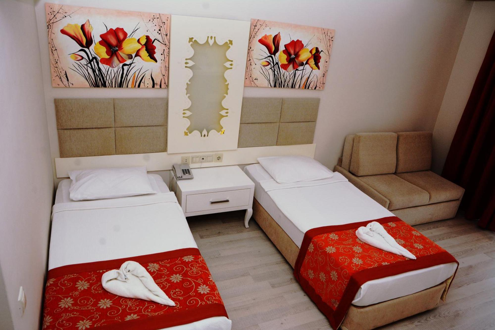 Miramor Hotel & Spa Antalya Extérieur photo The photo shows a hotel room featuring two single beds with white linens, each adorned with a decorative red throw. The headboards are upholstered in a light beige fabric. Above the beds, there are two large artwork pieces depicting colorful flowers.