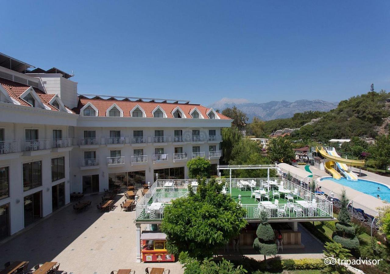 Miramor Hotel & Spa Antalya Extérieur photo The photo shows a hotel or resort facility with a well-maintained exterior. There is a large green area with grass and some trees, likely intended for relaxation or recreational activities. In the background, there are water slides suggesting an amus